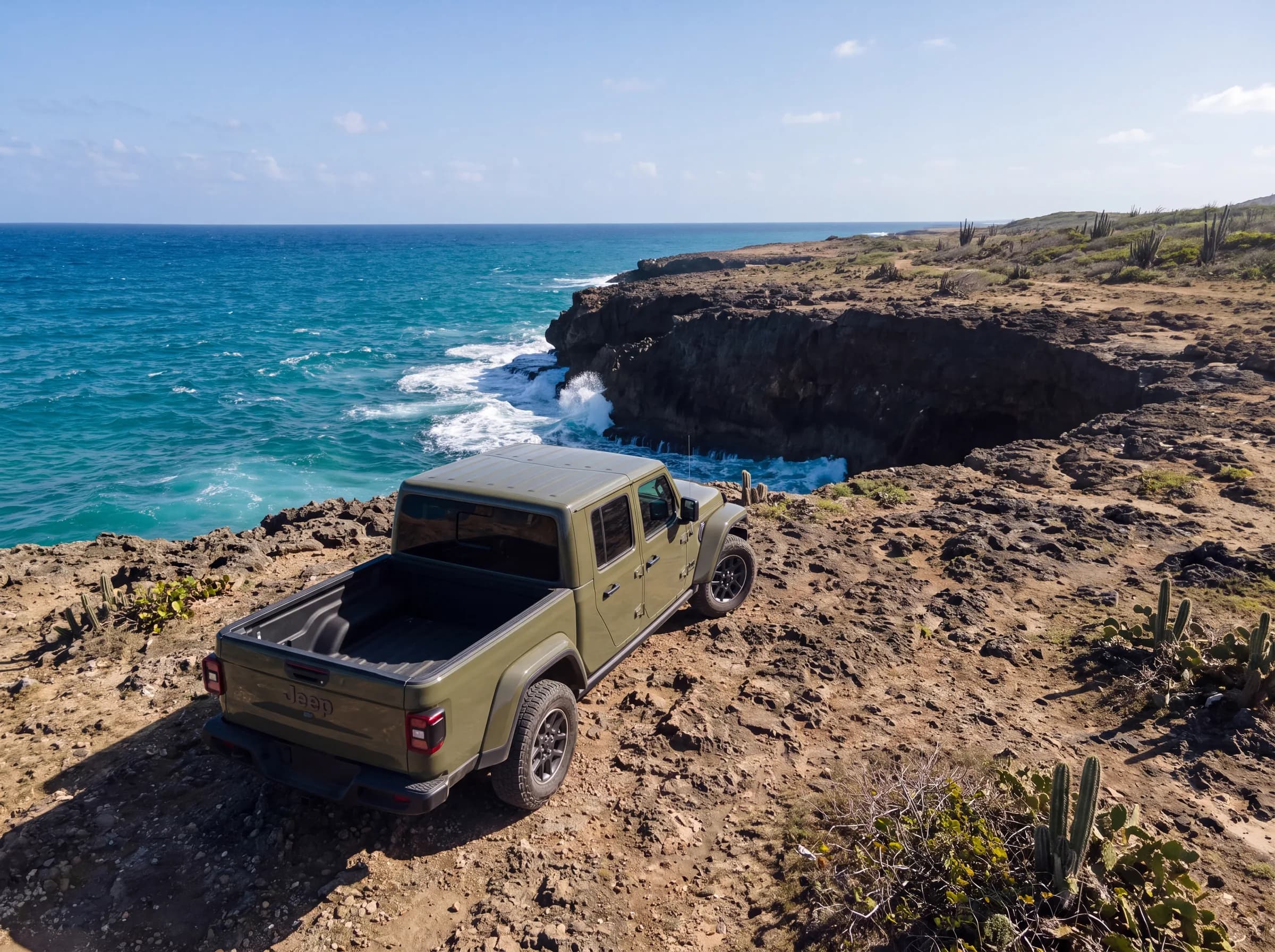 Olive green Jeep Gladiator pickup with the bed open, parked on a rocky headland above the surf in Aruba