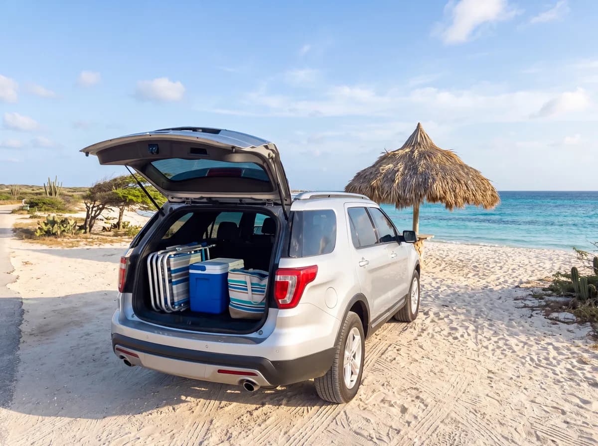 Silver SUV with the tailgate open and beach chairs and a cooler in the back, parked by a palapa on a white sand beach in Aruba