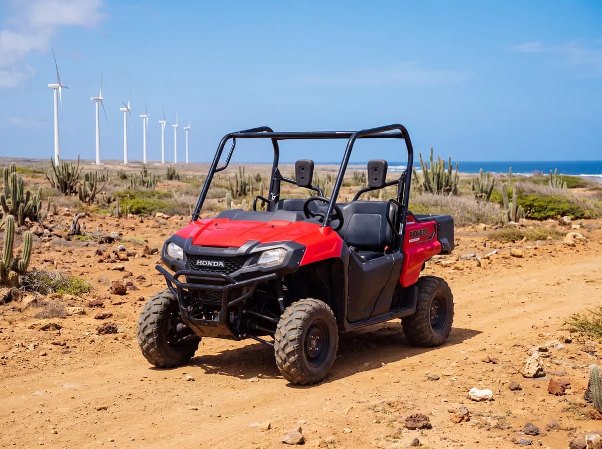 Red two-seat side-by-side UTV on a desert trail with cacti and the Aruba wind farm behind it